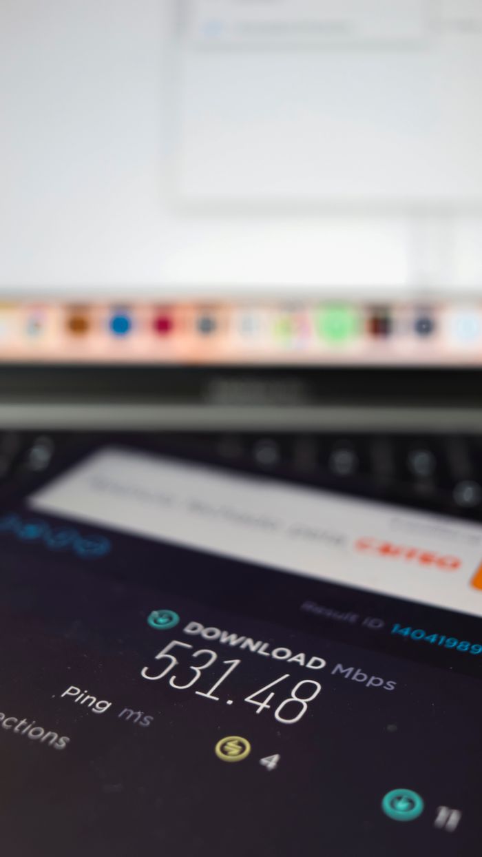 creative Close-up of a smartphone showing internet speed test results with a laptop in the background.