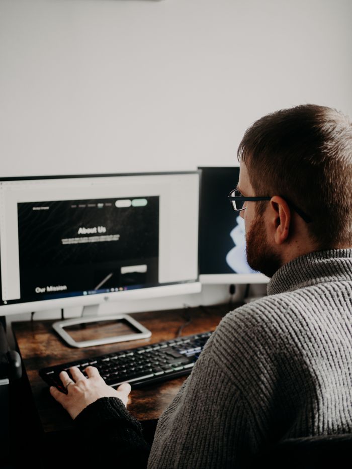digital Man working on web design at home office setup with dual monitors.