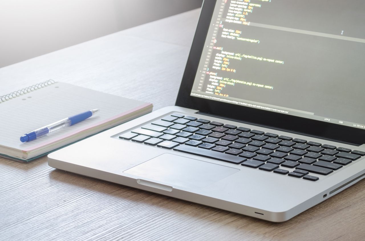 creative-02 Laptop with code editor open, notebook and pen on wooden desk, perfect for tech and work themes.