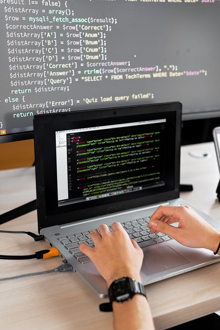 Crafting Captivating Headlines: Your awesome post title goes here Person coding at a desk with laptop and external monitor showing programming code.
